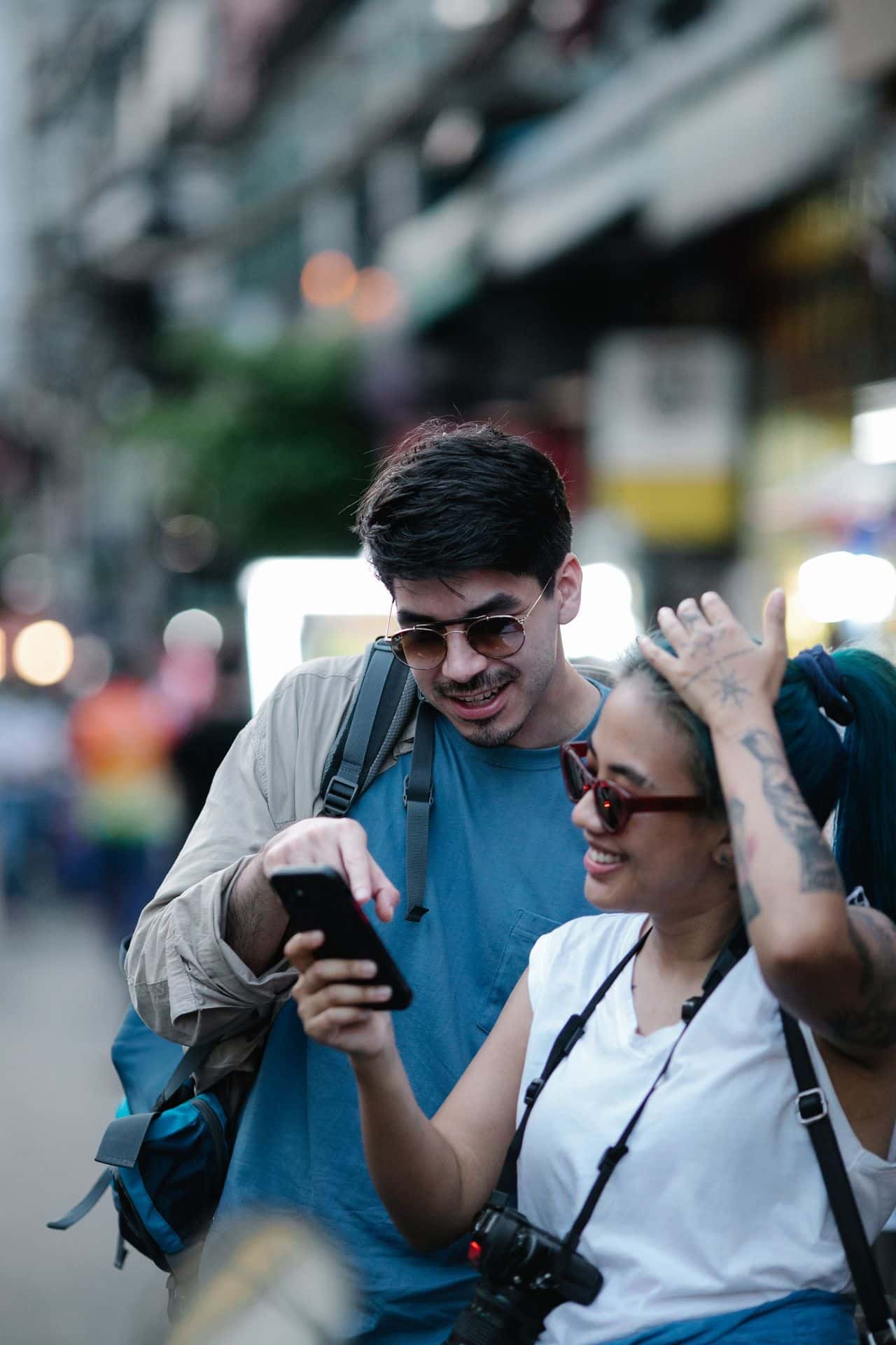 Casal de intercambistas sorrindo enquanto olha o celular em rua movimentada