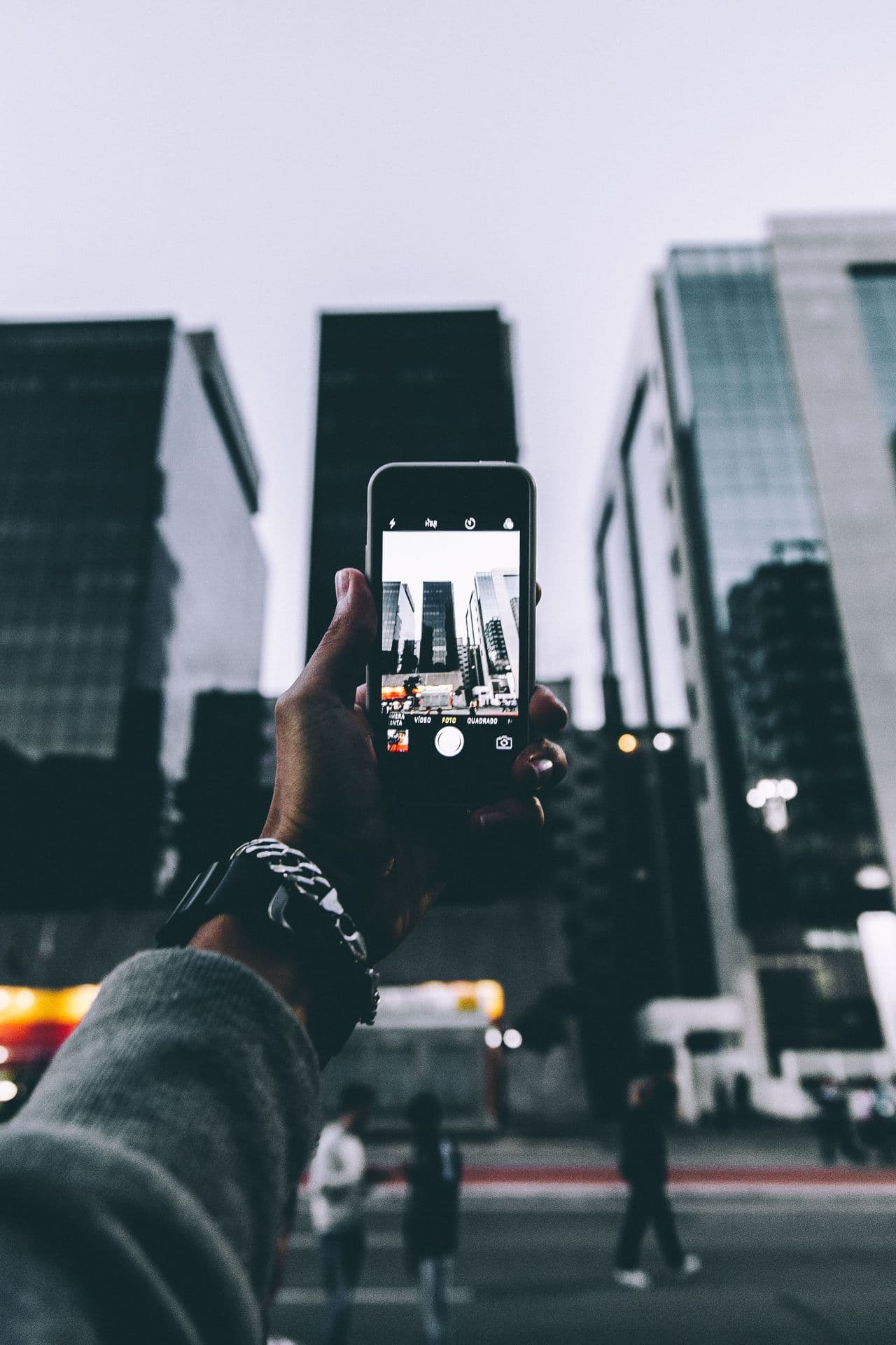 Mão segurando celular fotografando prédios de uma grande avenida à noite