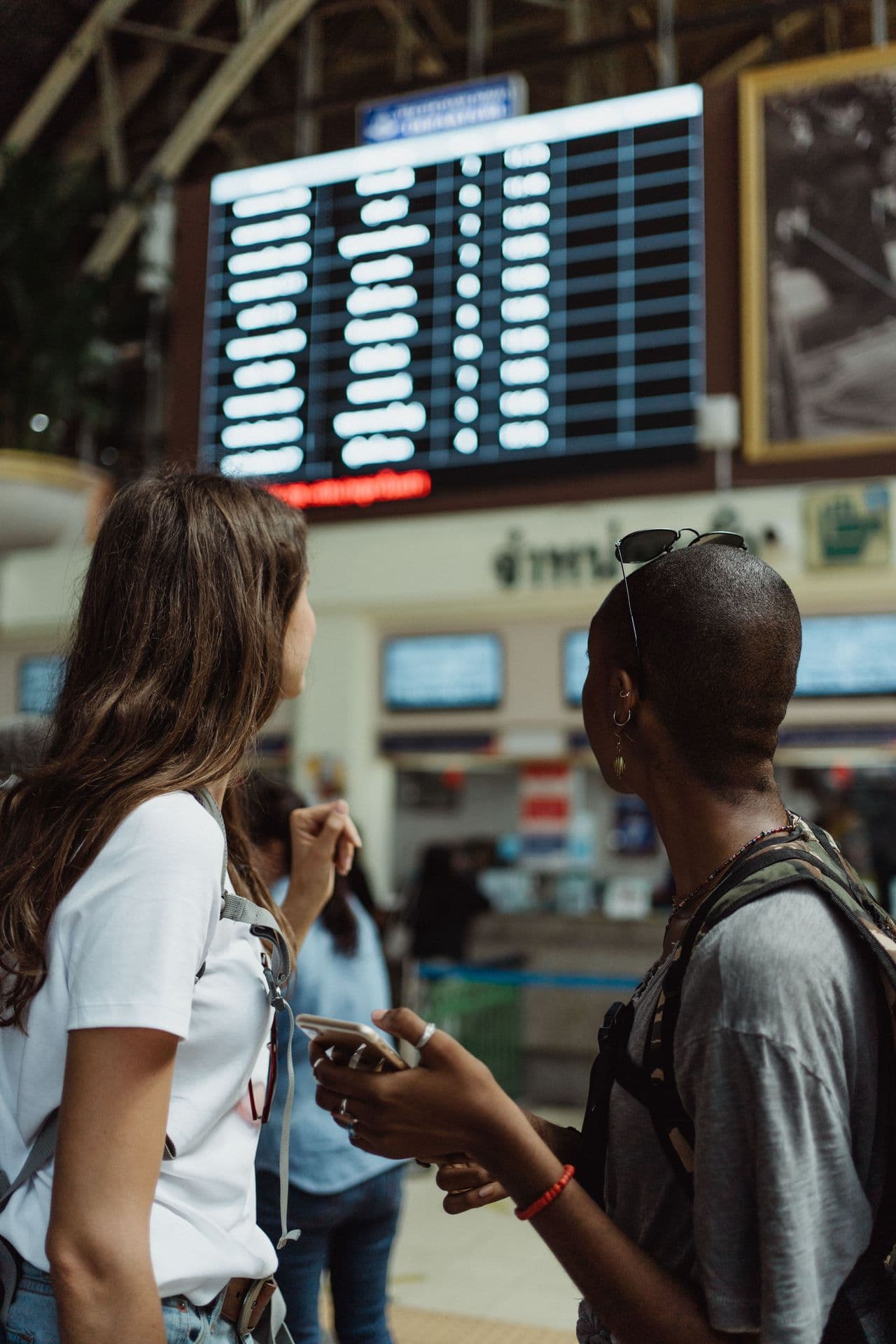 Dois viajantes conferindo o painel de partidas em uma estação